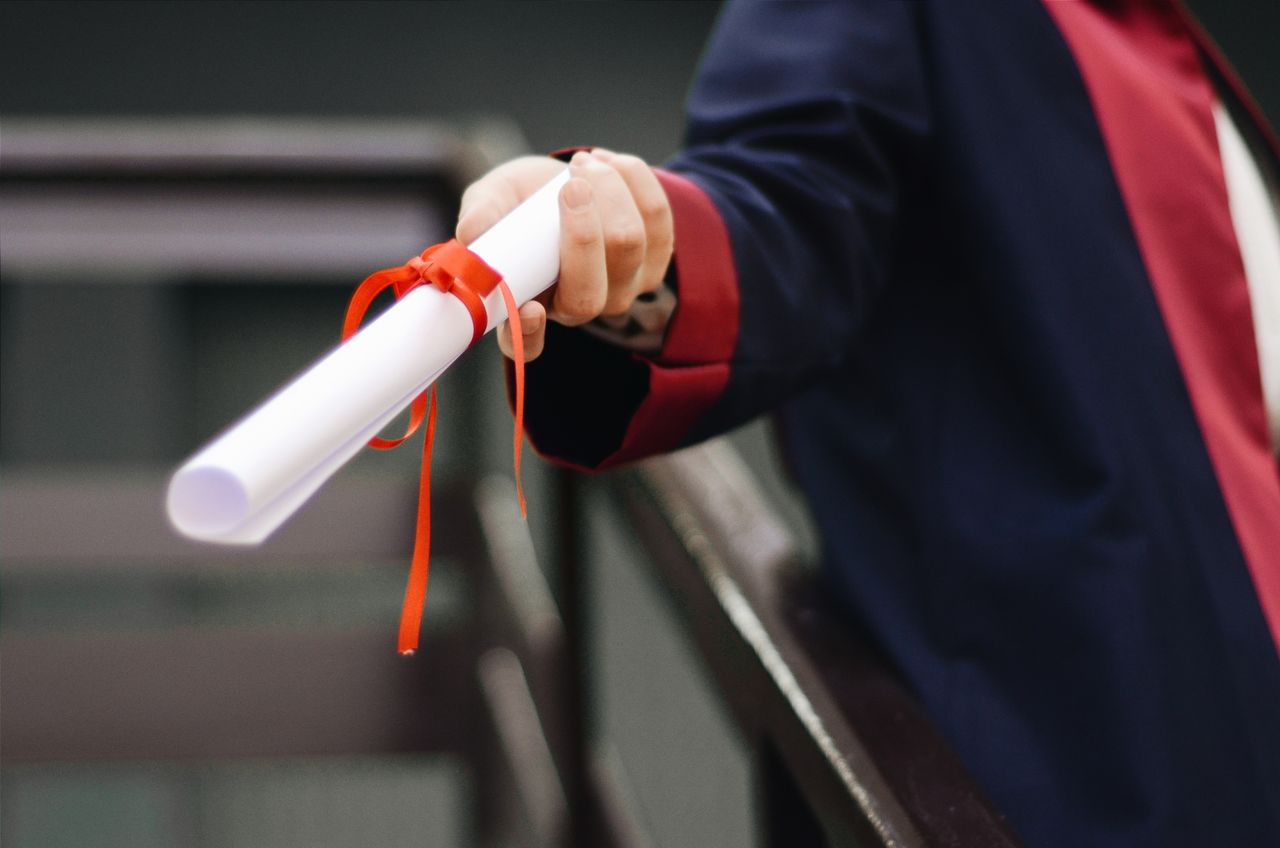 services-01 A close-up image of a graduate holding a diploma tied with a red ribbon, symbolizing achievement and success.