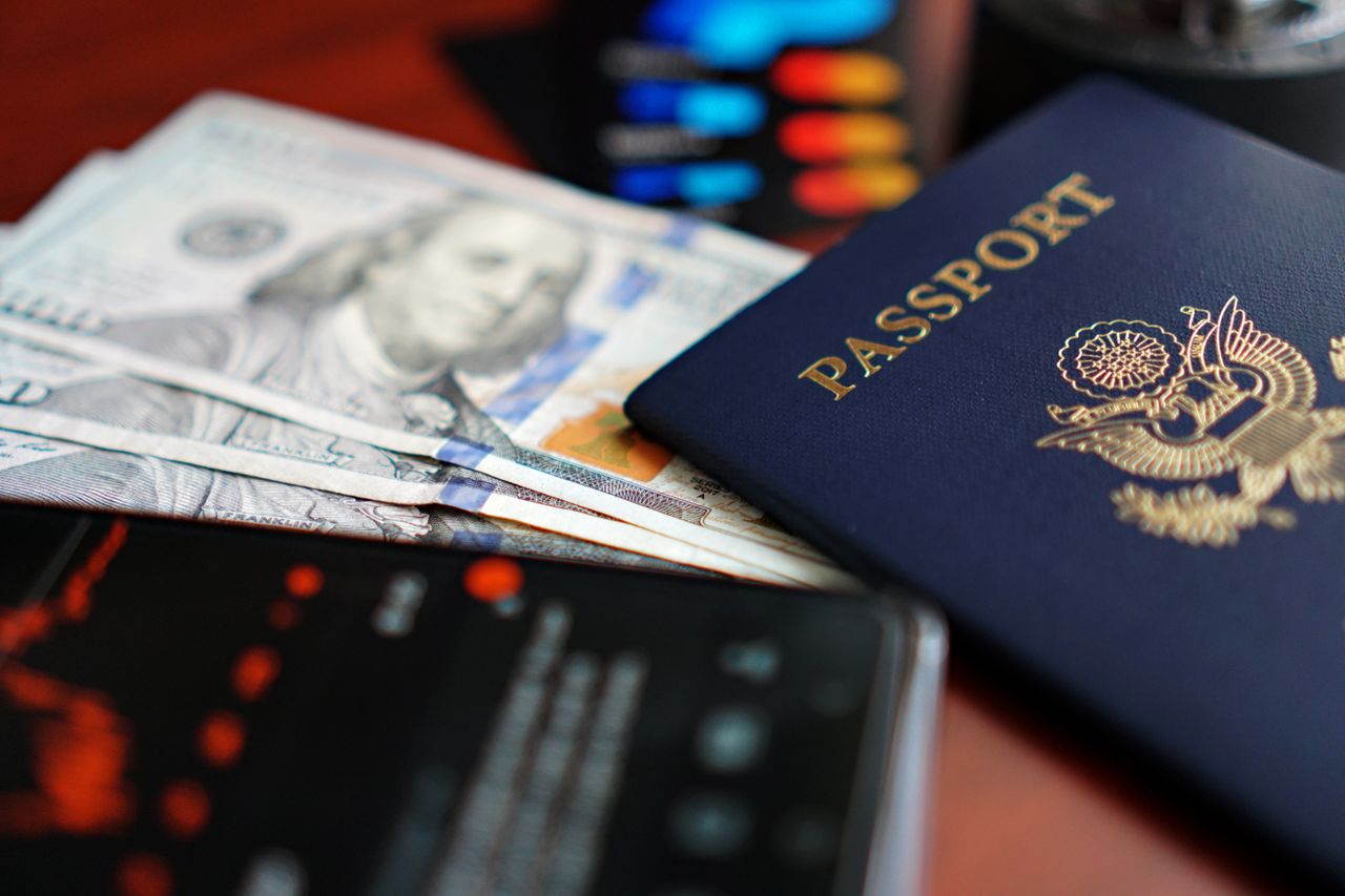 ours-journey A close-up image of a U.S. passport, dollar bills, and a smartphone.