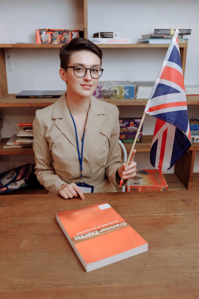 about-02 Portrait of a woman with eyeglasses holding a Union Jack flag at a desk.