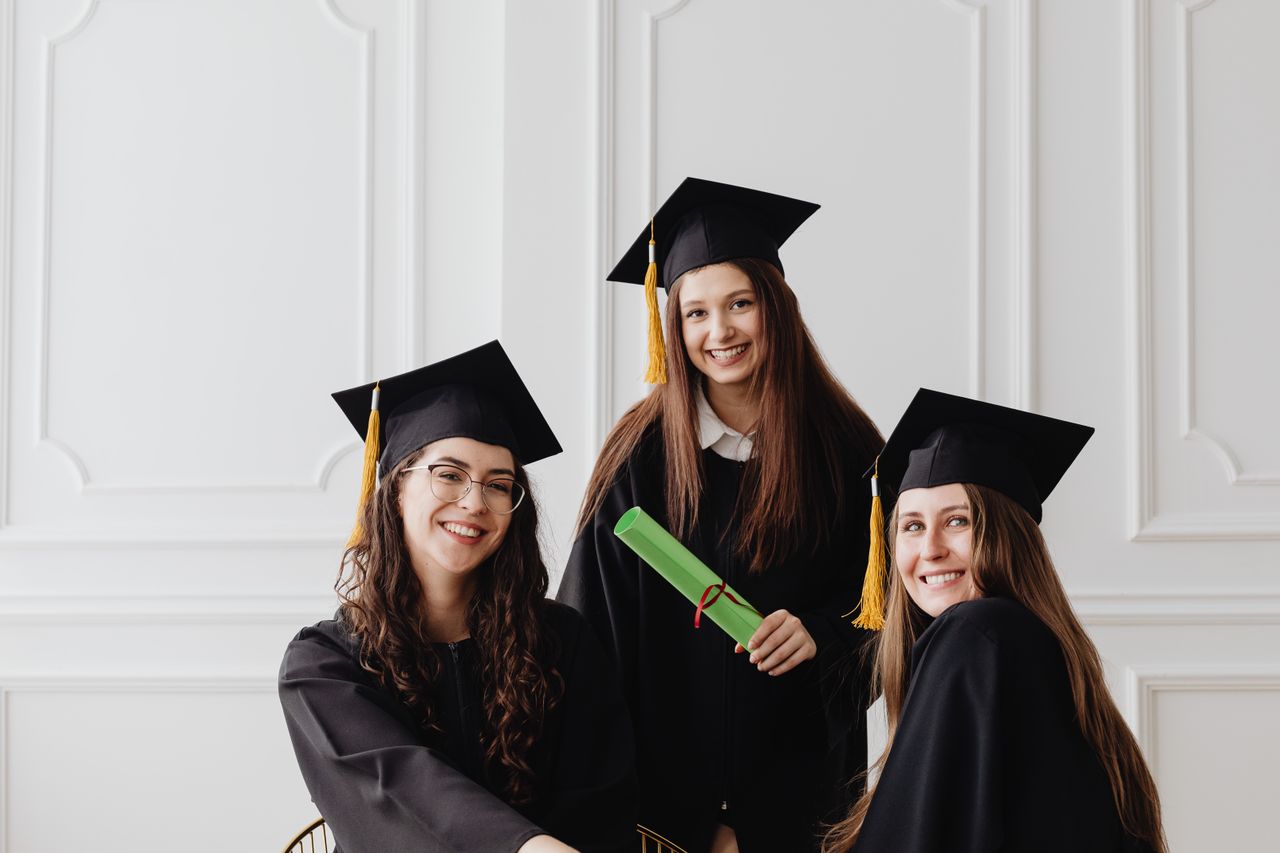 services-img Three young women celebrating graduation with caps and diplomas indoors.